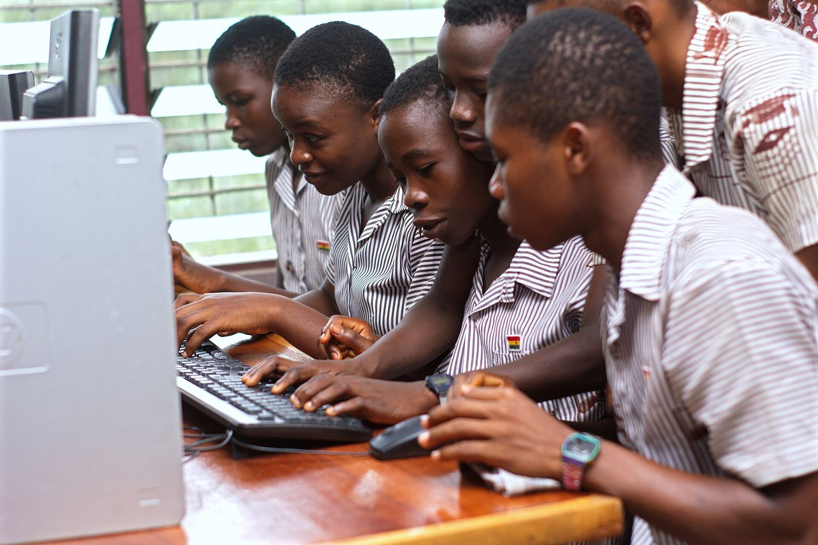 six learners gathered around a single shared desktop computer