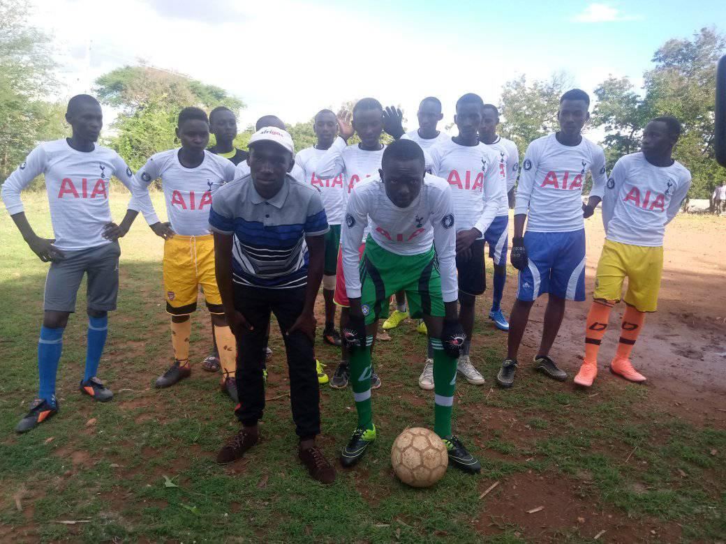 a Kenyan youth football team posing with their coach on a dirt pitch